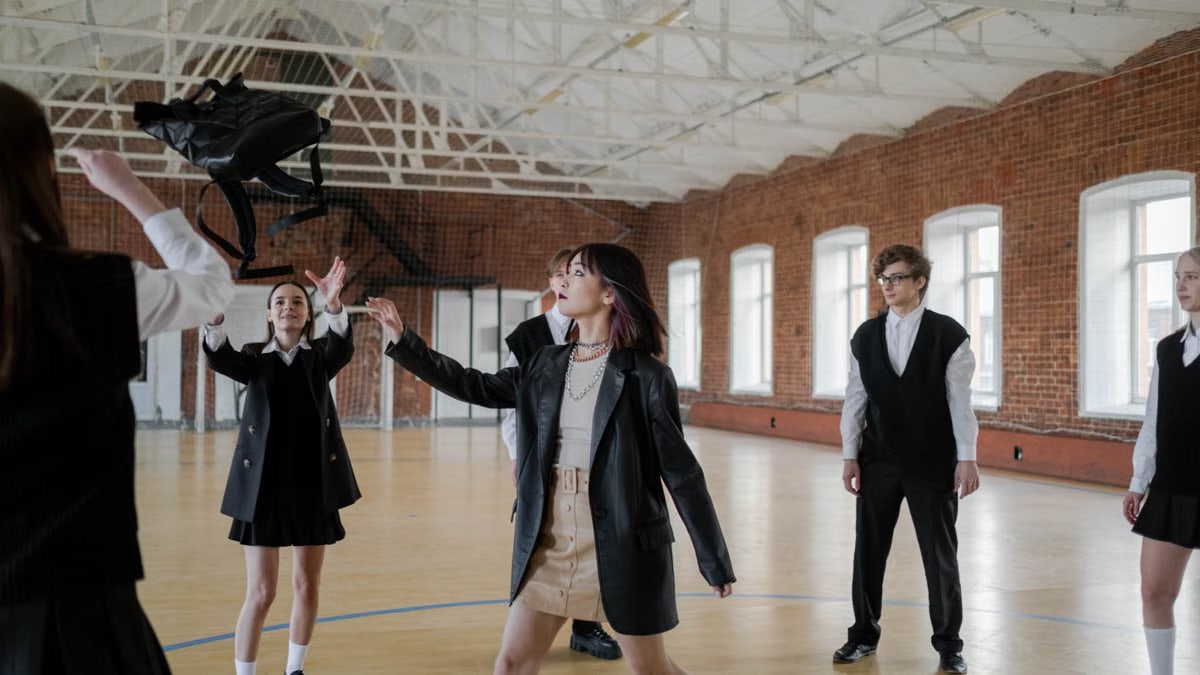 High school students in uniforms throwing a backpack in a gym, showcasing youth camaraderie.